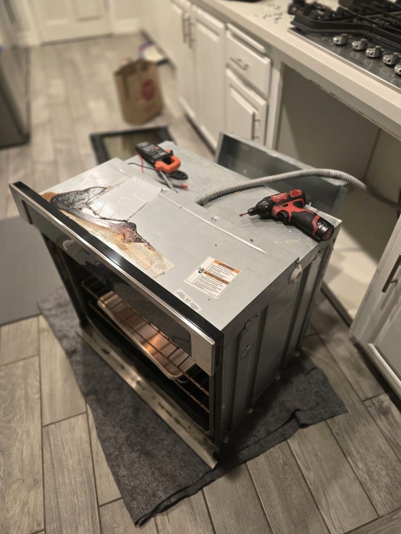 Wall oven pulled from cabinet for repair with Milwaukee drill and multimeter